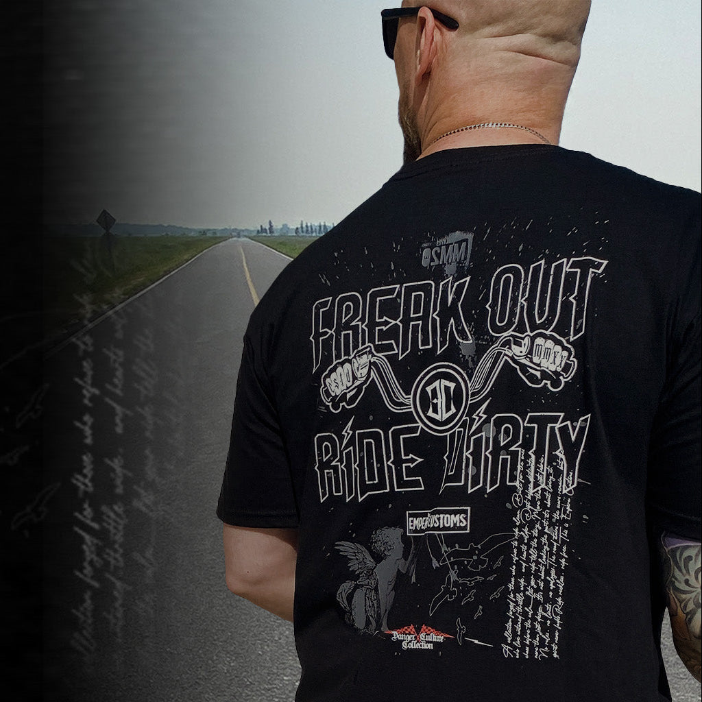 Man wearing a black t-shirt with graphic designs and text, standing on a road.